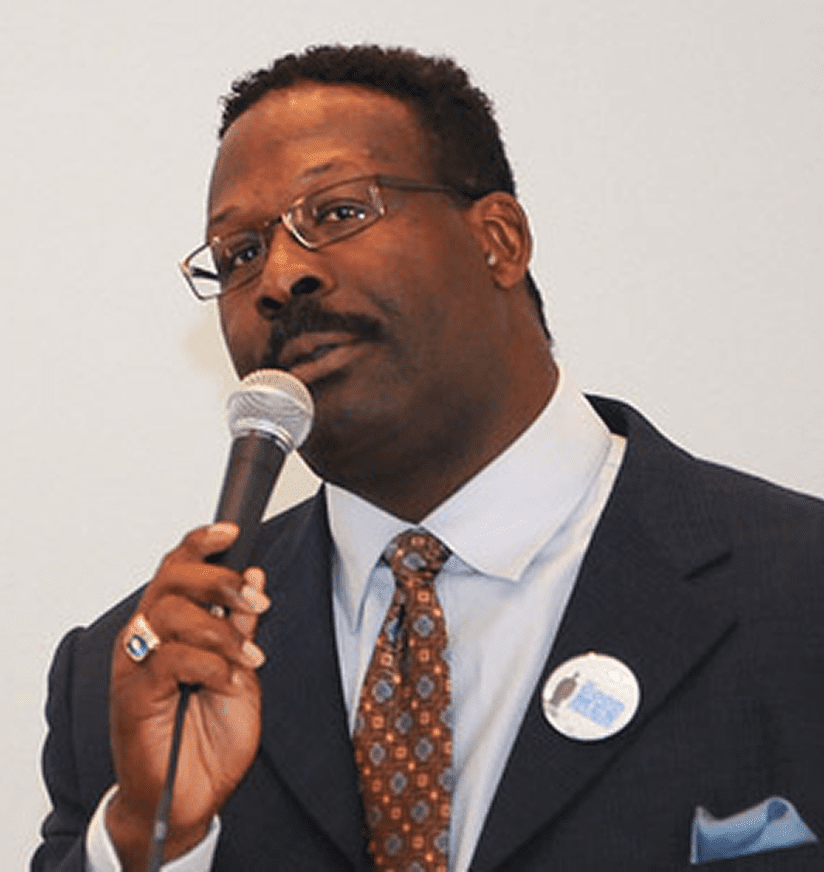 Man in suit and glasses speaking into microphone