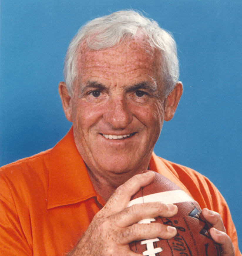Smiling older man in orange shirt holding football