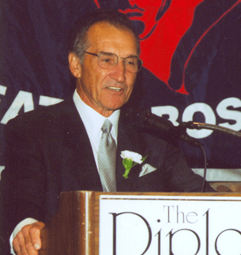 Older man speaking at podium with boutonniere